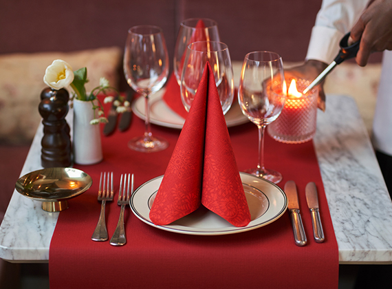 Folded red Ornamental napkin on a matching red table runner.